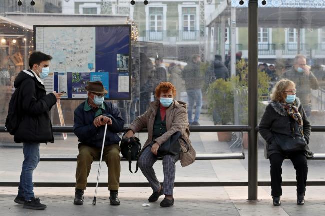 People wearing face masks to curb the spread of Covid-19 sit at a bus stop in Lisbon, Portugal (Ana Brigida/AP)